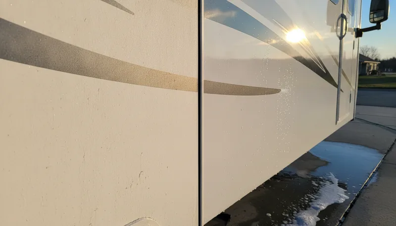 Close-up of an RV fiberglass sidewall showing dull chalky oxidation on one half and glossy polished finish on the other, demonstrating RV fiberglass detailing results.