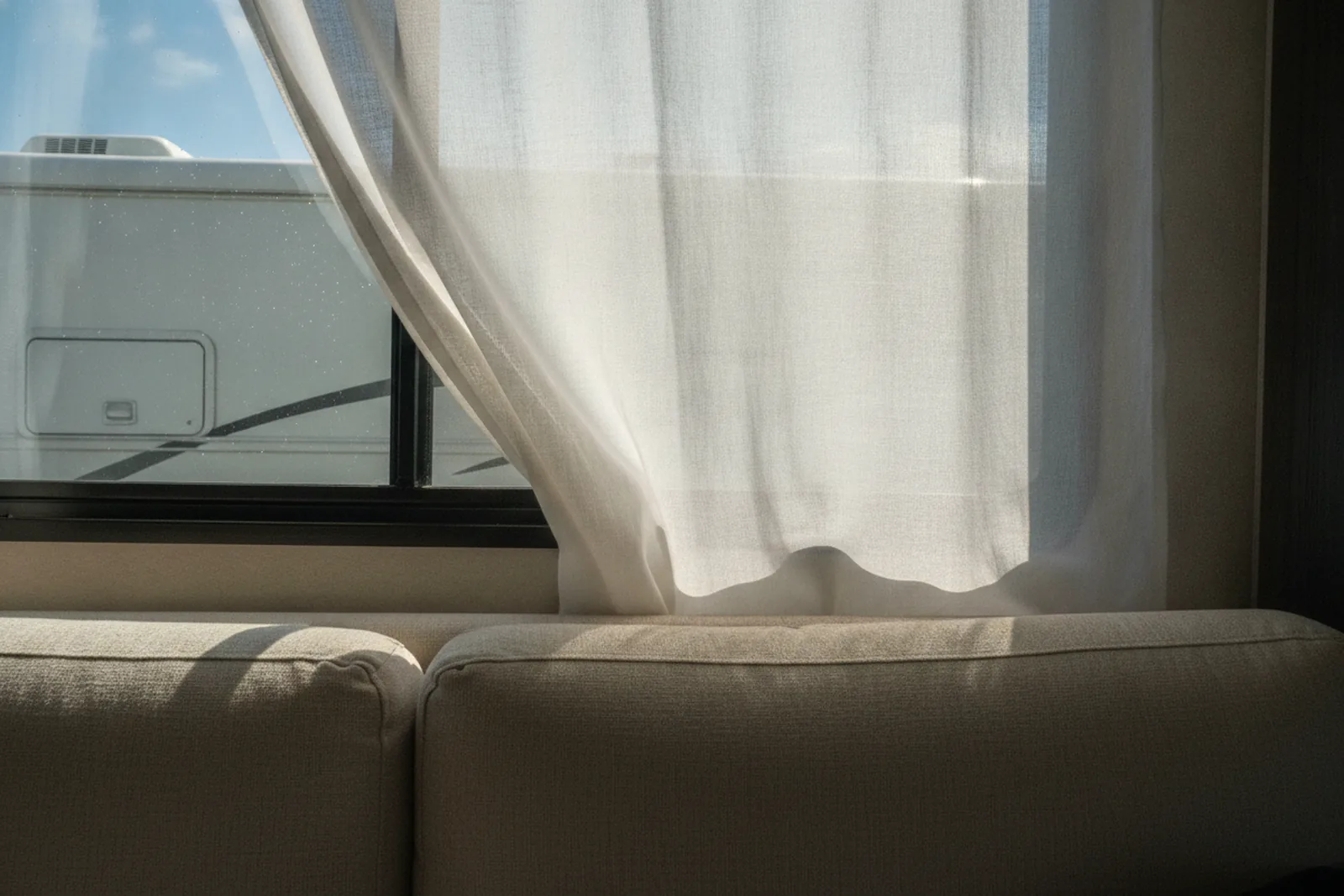 Open RV window with breeze moving curtain over clean sofa after RV interior detailing.
